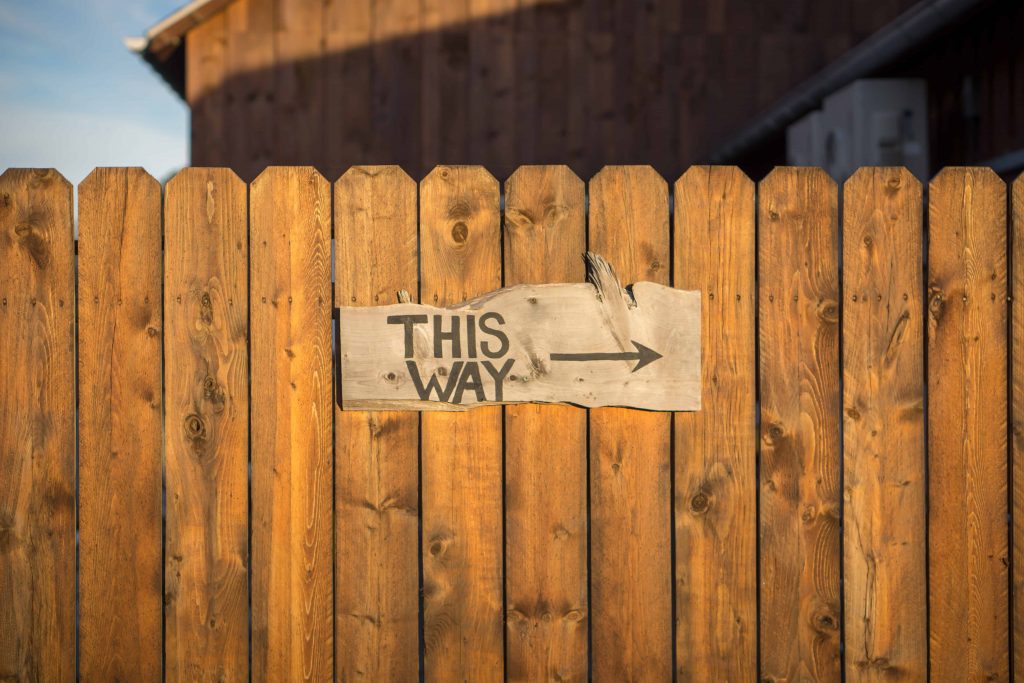 Wood fence with sign This Way representing how to get rich with a normal job